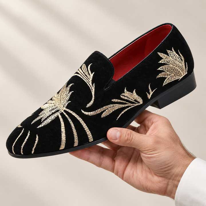 Alessio loafers in black with gold embroidery, held in a hand.