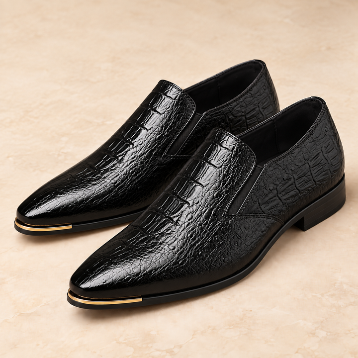 Callum black crocodile-embossed pointed loafers with gold-tone toe trim, photographed as a pair in a warm neutral studio.