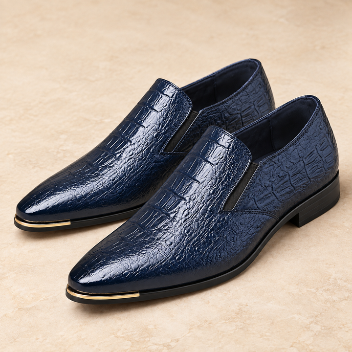 Callum deep navy blue crocodile-embossed pointed loafers with gold-tone toe trim, photographed as a pair in a warm neutral studio.