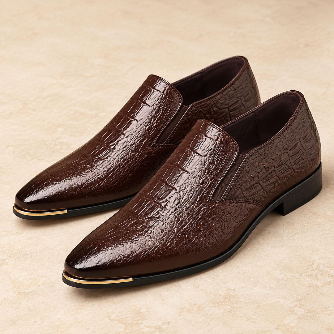 Callum dark brown crocodile-embossed loafers with pointed toes and gold-tone trim, photographed as a pair in a warm neutral studio.