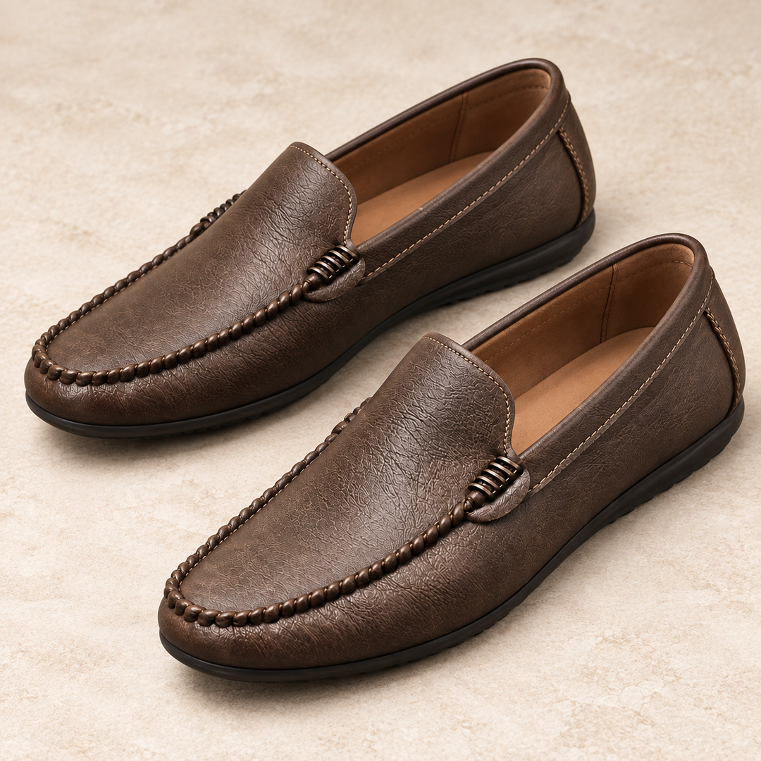 Close three-quarter studio view of Ronan brown moc-toe loafers showing the braided apron stitching and vamp ornament.
