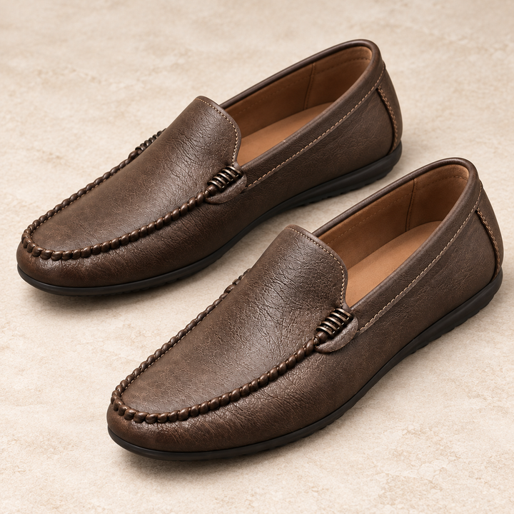 Close three-quarter studio view of Ronan brown moc-toe loafers showing the braided apron stitching and vamp ornament.