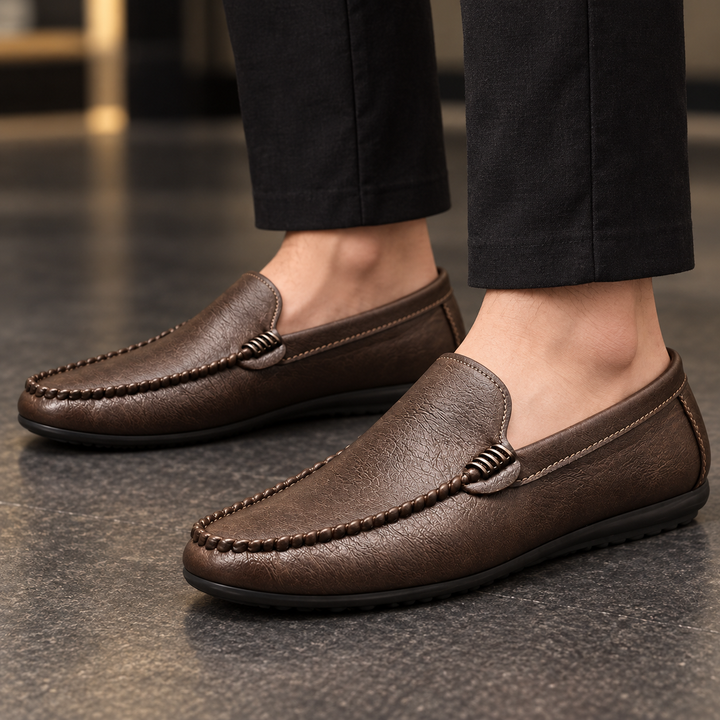 Ronan brown moc-toe loafers worn with tailored trousers, framed closely around the shoes and ankles.