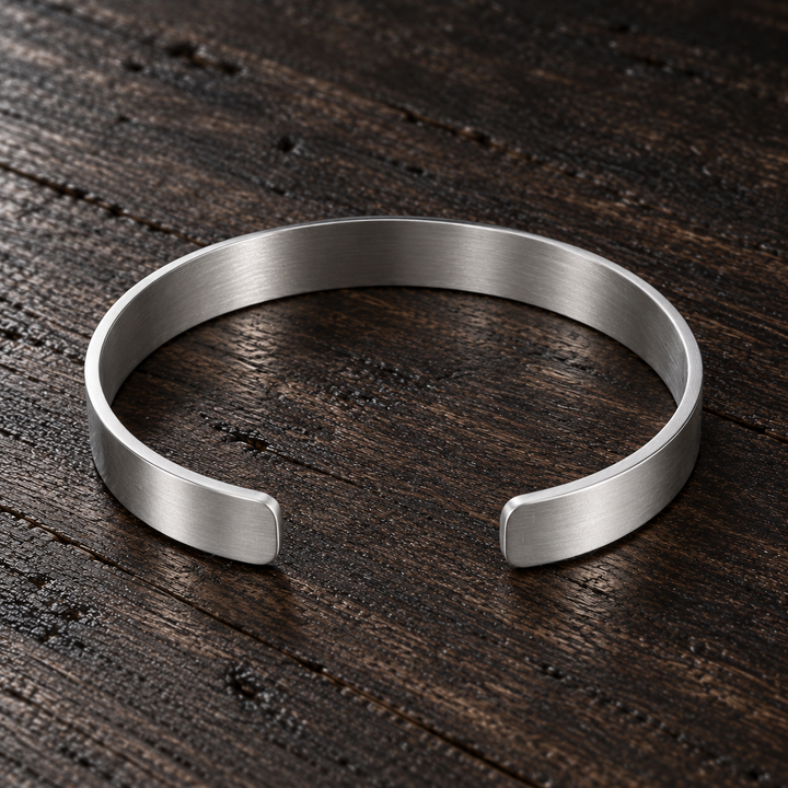 The Mayfair sterling silver open cuff with a brushed finish, lying flat on dark wood